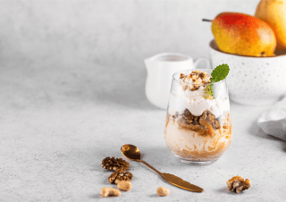 Birnen-Haselnuss-Dessert mit Karamell im Glas mit CremiG Vanille auf einem Tisch mit Birnen und Nüssen